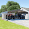 A Large Metal Carport Kit Providing Shelter For Two Vehicles, With A Black Galvanized Steel Roof And A 2X2 Steel Tube Frame, Displayed On A Gravel Surface Next To A Residential Building. - Saksby Wholesale