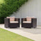 Two Wicker Chairs With Beige Cushions On A Patio Area With Greenery And A Wooden Wall.