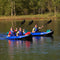 Three People Paddling A Blue Kayak On A Calm Lake With Trees In The Background - Saksby Wholesale