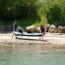 Two People Carrying A Kayak On A Rocky Shoreline With Trees In The Background - Saksby Wholesale