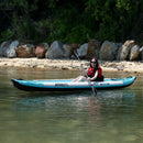 Person Paddling A Sea Eagle Kayak On A Calm Body Of Water With A Rocky Shoreline And Greenery In The Background. - Saksby Wholesale