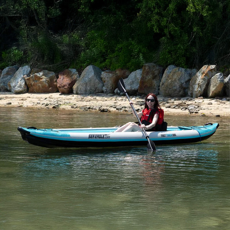 Person Paddling A Sea Eagle Kayak On A Calm Body Of Water With A Rocky Shoreline And Greenery In The Background. - Saksby Wholesale